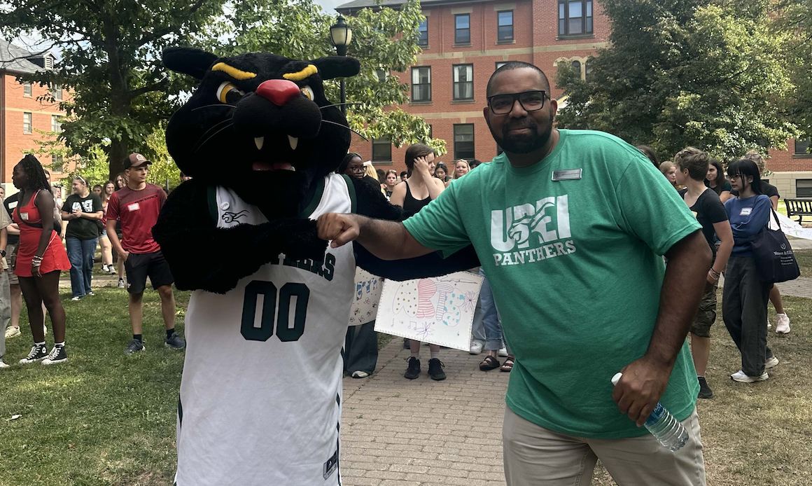 Photo of mascot and man fist bumping in front of large crowd