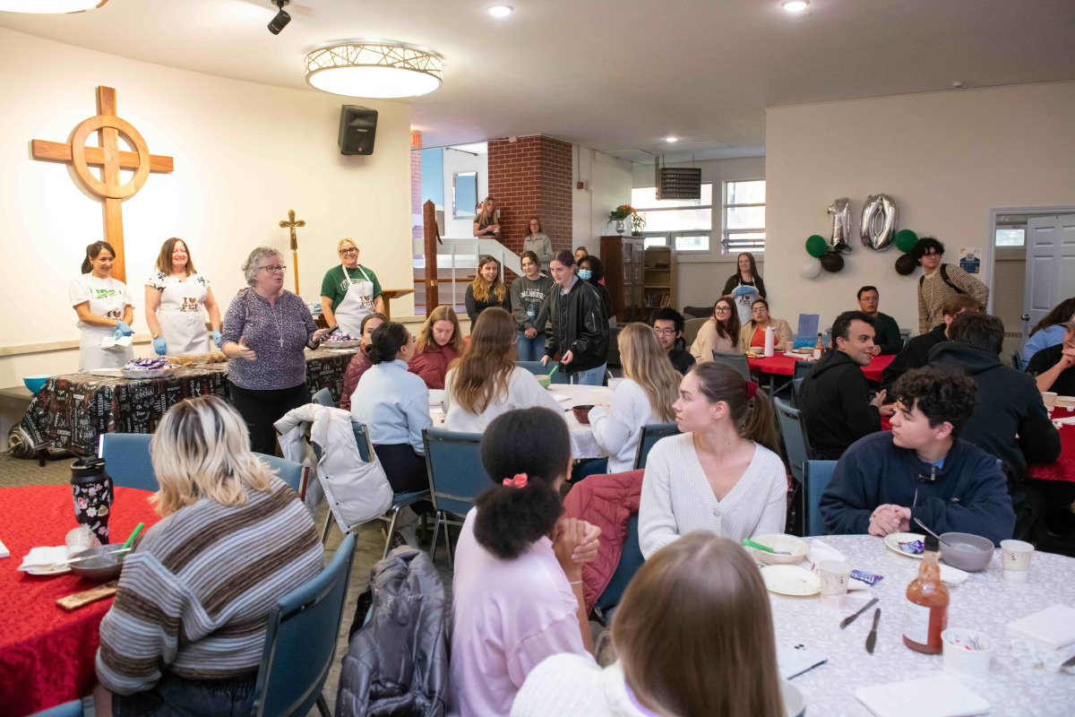 Large crowd of students sitting at round tables listening to woman speaking