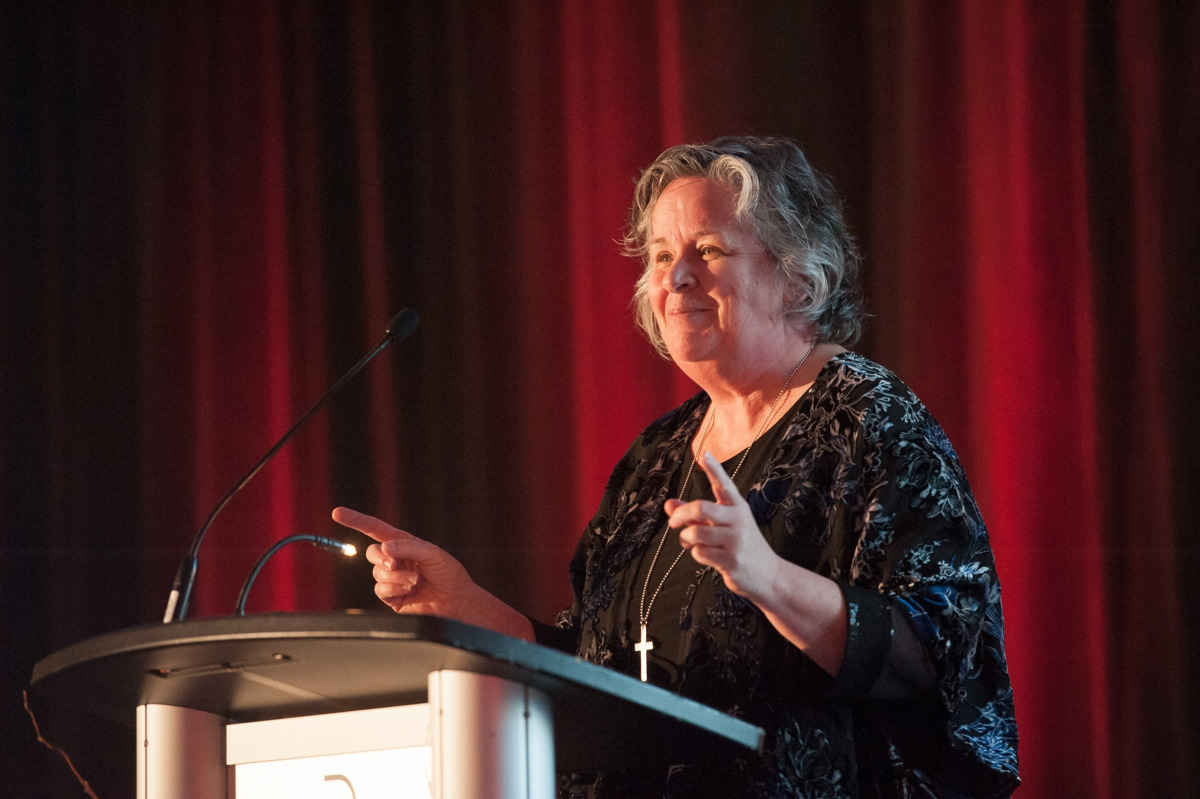 Woman standing at podium pointing her index fingers.