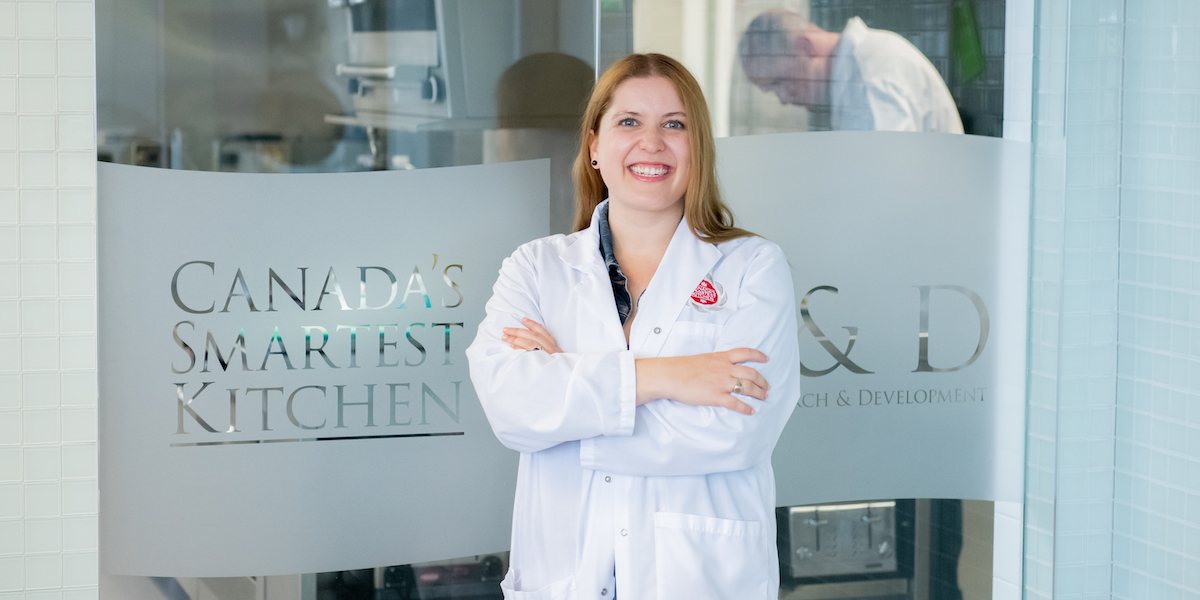 female posing in front of laboratory window with writing on it reading Canada's Smartest Kitchen