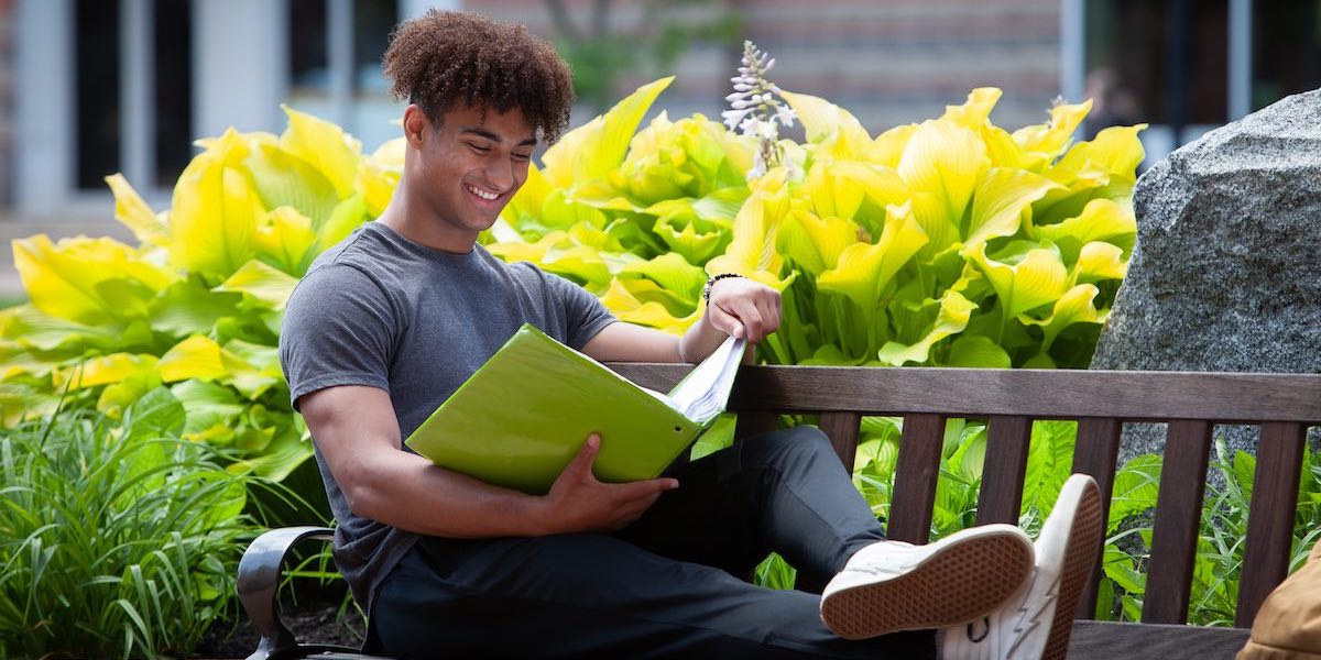 jeremy norman seated on a park bench at upei reading a textbook