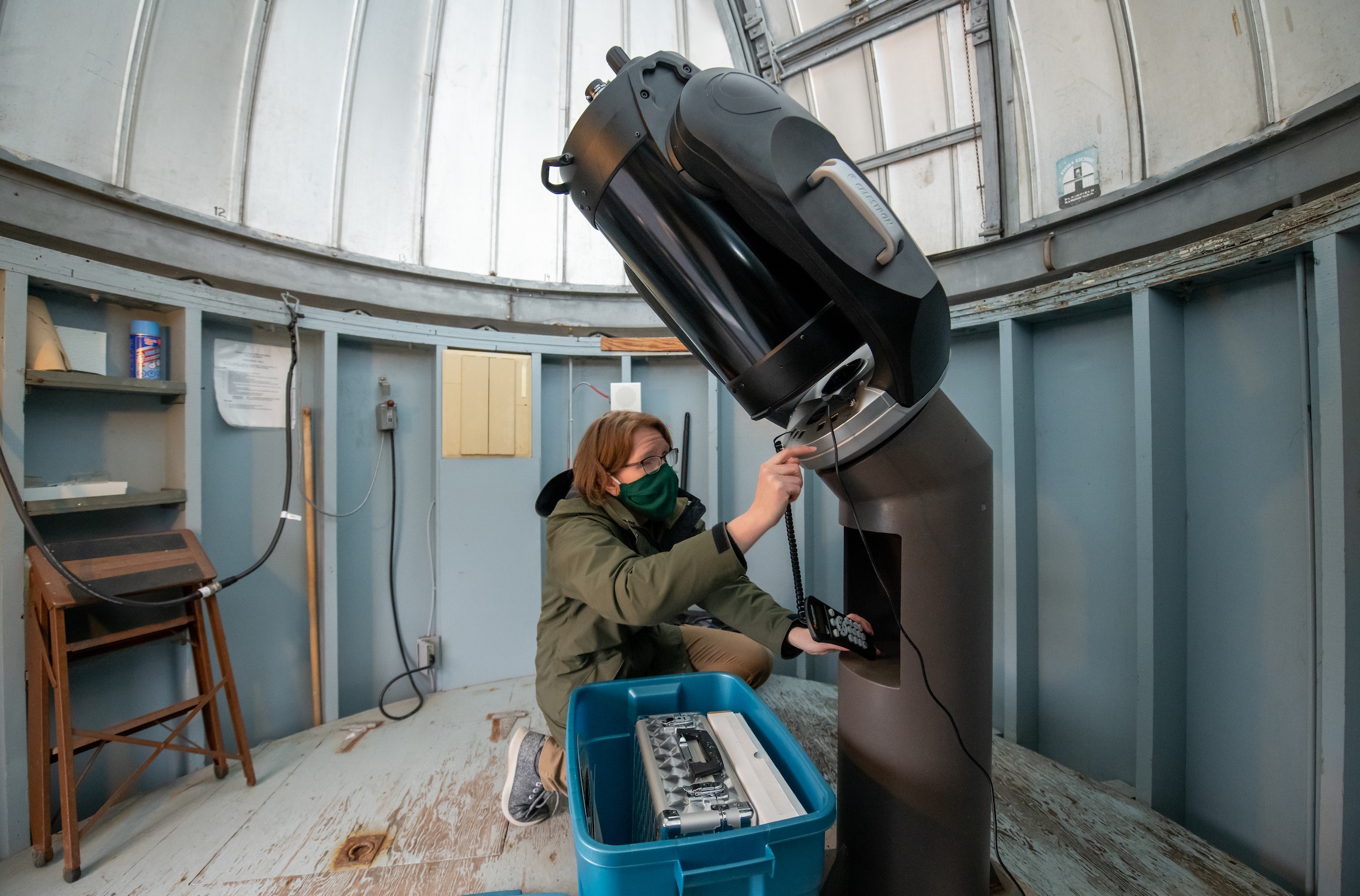 A woman manipulates a shiny black telescope inside of a small room with a domed roof