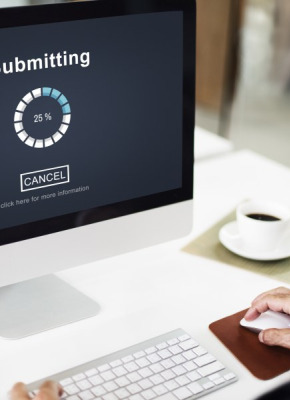 Photo of man sitting at a desk in front of a computer submitting an online form