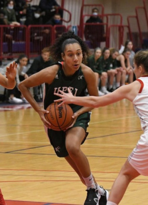 A femal baksetball player in green Panthers gear charges towards the basket in a game