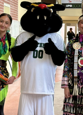 Two young women wearing Mi'kmaw regalia meet up with the UPEI mascot