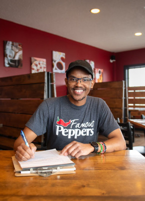 a smiling man sitting at a restaurant table writing on a clipboard