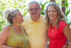 Two smiling women flank a smiling older man no a sunny day. All look happy and relaxed.