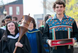 Photo of person carrying ceremonial mace and person carrying Eagle Feather leading a procession