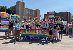 Photo of large group of people holding a banner and wearing clothing in bright rainbow colours