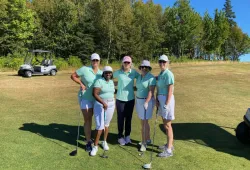 photo of five women wearing green shirts, standing on a golf course