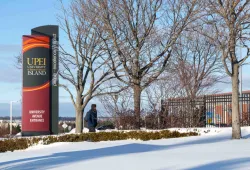 Student walking by sign at the entrance of University in winter
