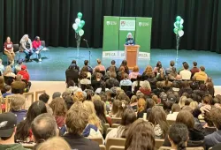 Photo of woman speaking at a podium on stage before a large audience