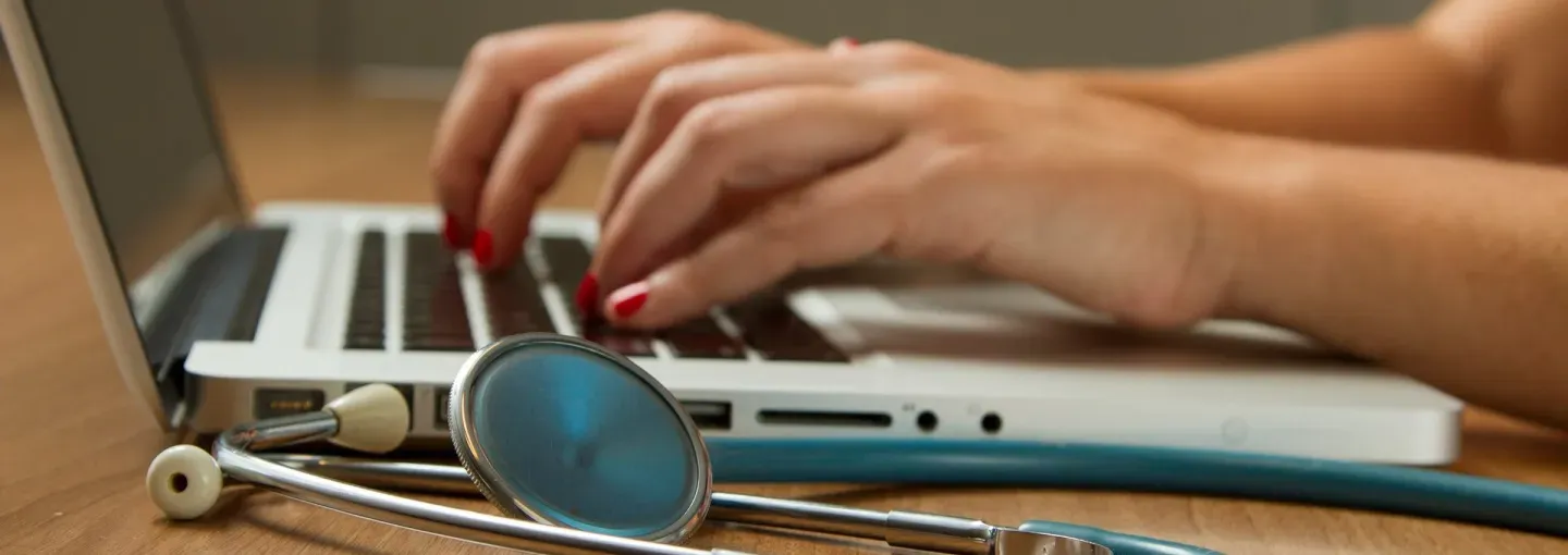 a stethoscope in front of hands typing on a keyboard 