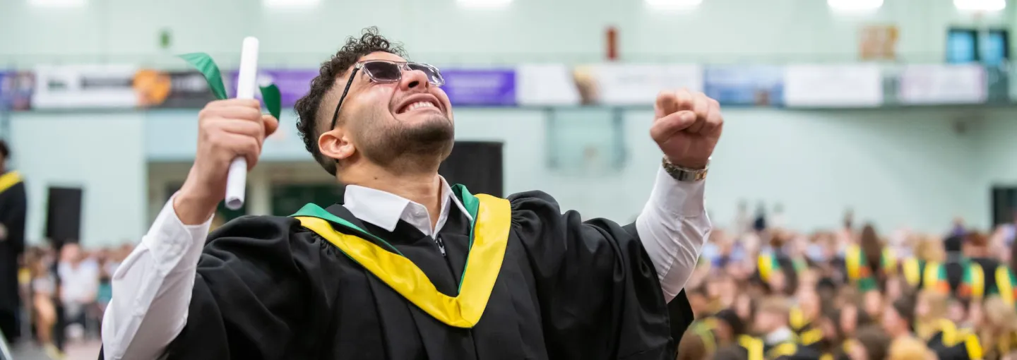 an excited graduate smiling holding a diploma scroll