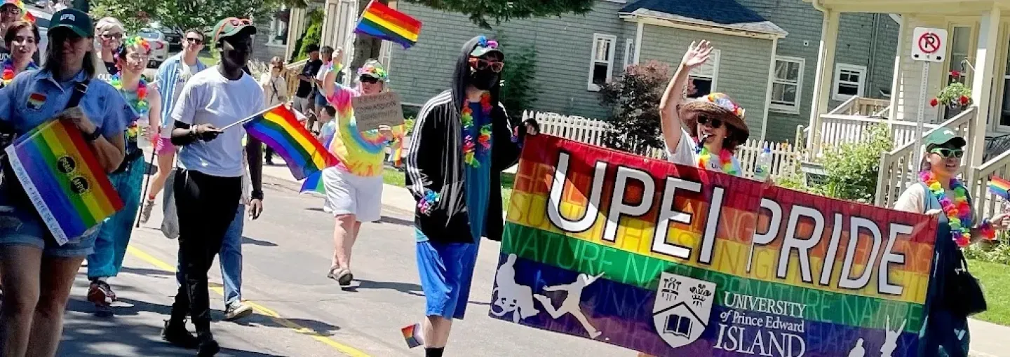 a group of people in a parade procession with a rainbow banner