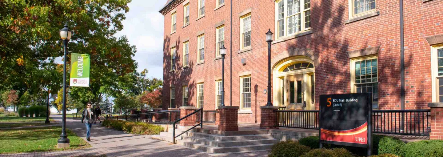 a student walking by the front facade of SDU Main Building at UPEI