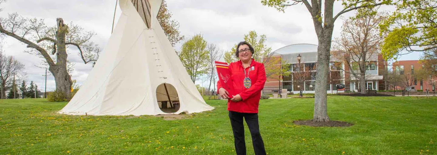 a person wearing red holding a red panel in front of the tipi at UPEI