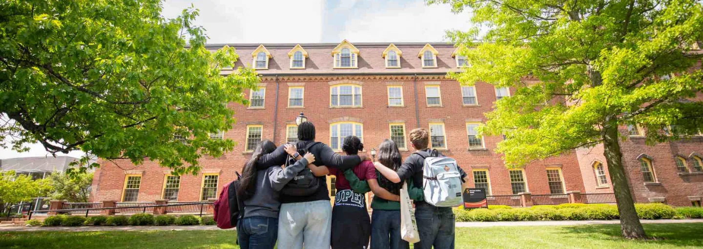 five students standing looking at a large brick building