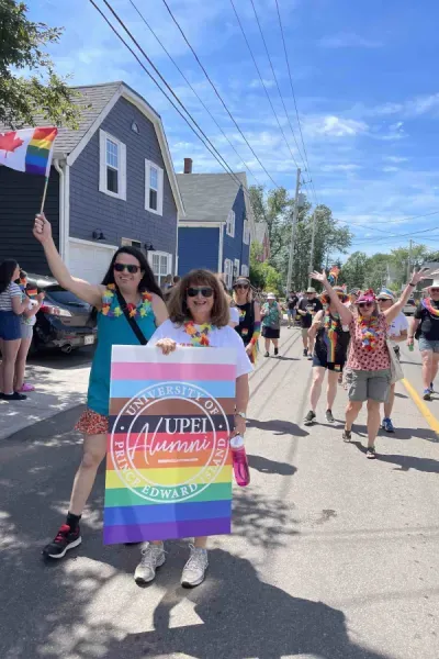 two people holding a UPEI Alumni flag in Progress Pride flag colours