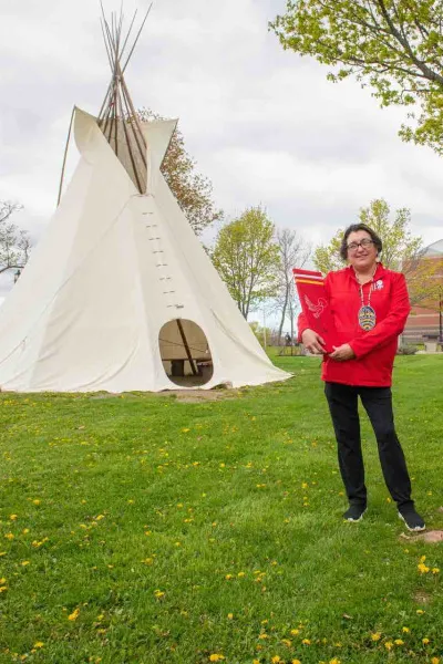 a person wearing red holding a red panel in front of the tipi at UPEI