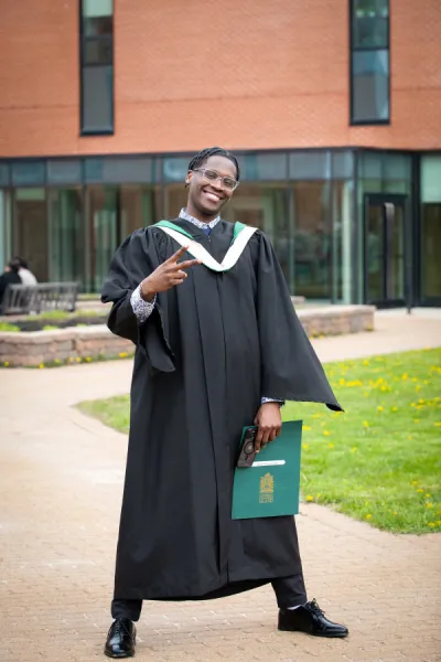 a smiling UPEI graduate in a black gown and green and gold hood