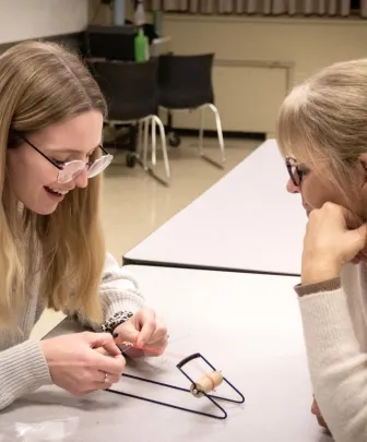 two people in a classroom using a small loom