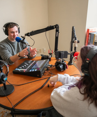 two students wearing headphones while speaking into microphones