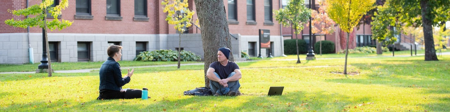 two students sitting in the UPEI quad with a large brick building in the background