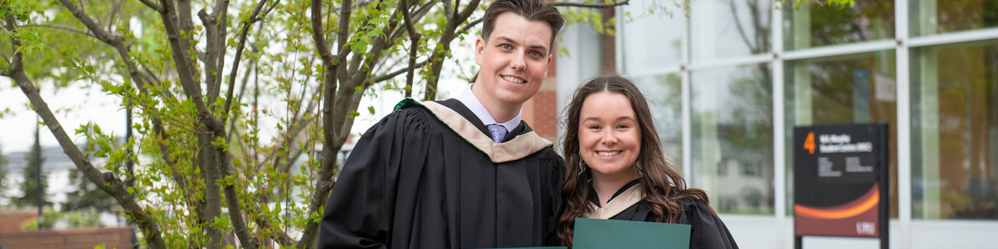 two UPEI graduates holding their degrees