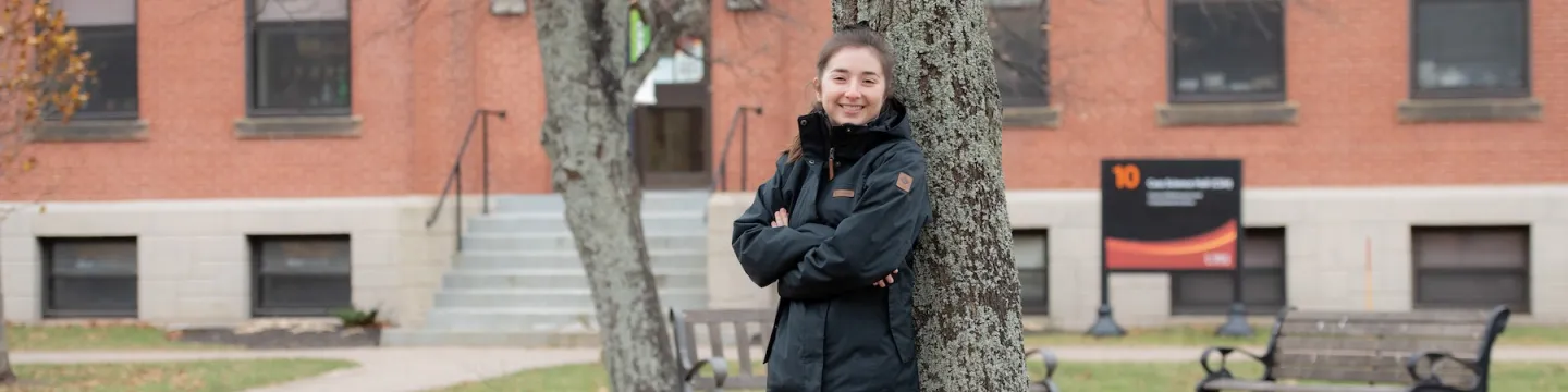 upei math graduate shannan hill leaning on a tree in front of cass science hall