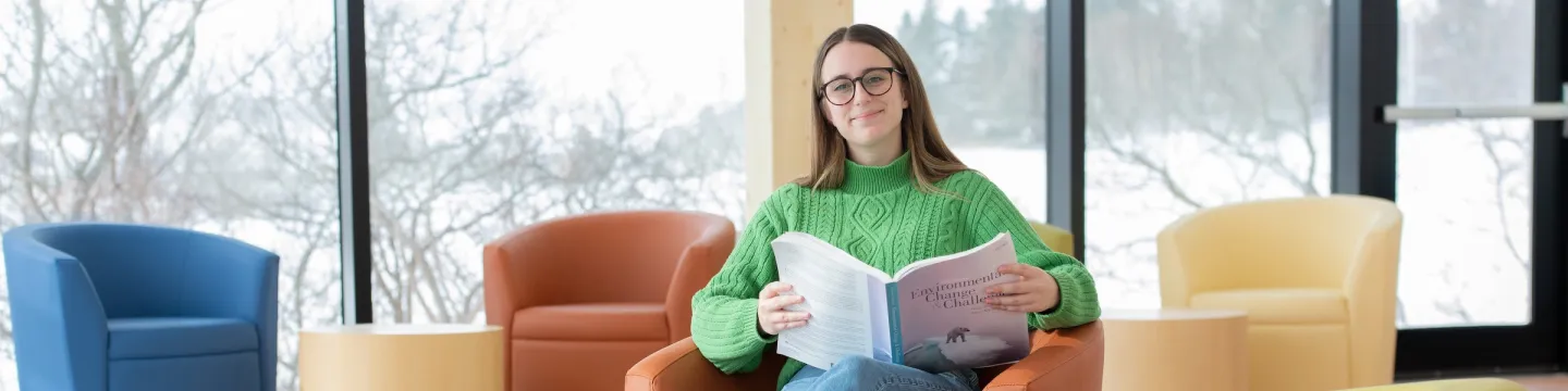 UPEI climate change student Zoe Furlotte reading a textbook with bright windows in the background