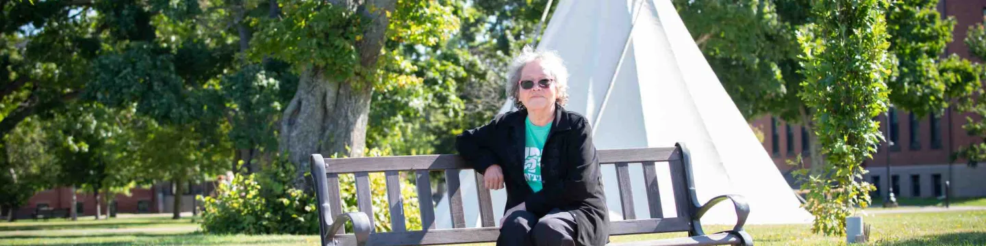 Dr. Angelina Weenie seated on a bench by the tipi in UPEI's quad