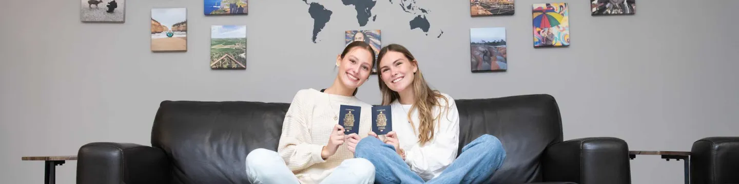 two students holding passports in front of photos of other countries