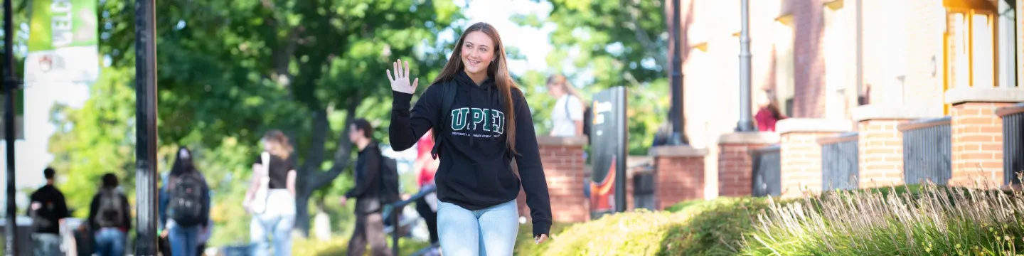 a smiling student waving in the UPEI quad