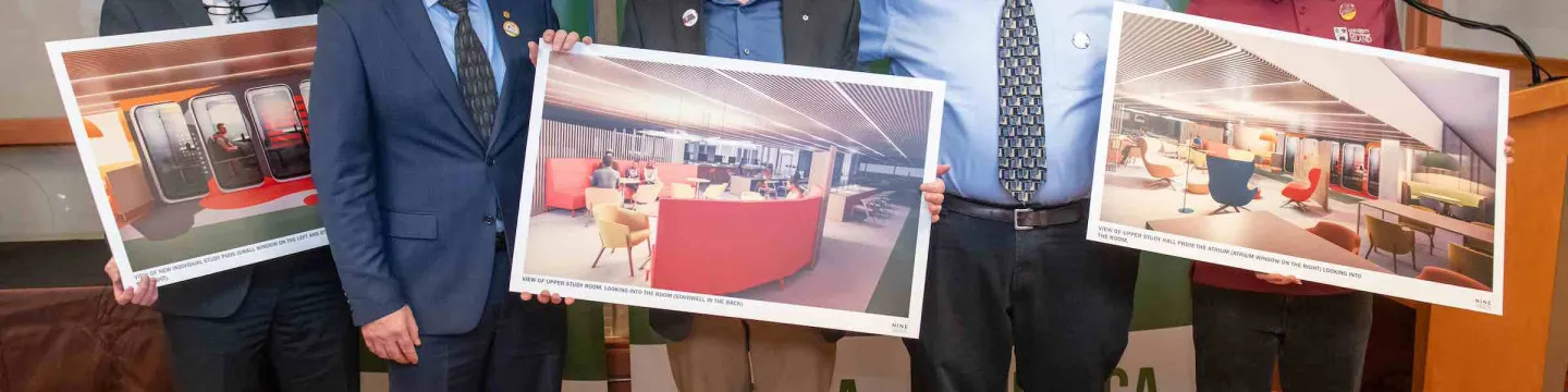 five men in the Robertson Library holding large prints of construction renderings
