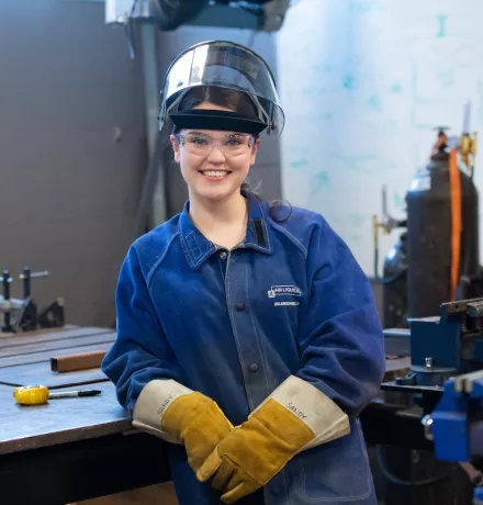 upei engineering student bridget patterson wearing a welding helmet, jacket and leather gloves