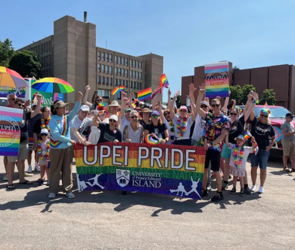 Members of the UPEI community at the 2024 PEI Pride Parade Photo of large group of people holding a banner and wearing clothing in bright rainbow colours